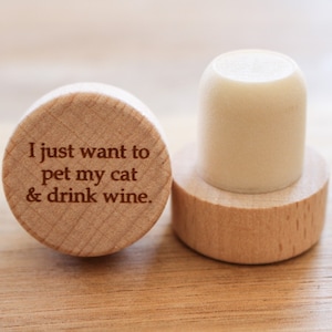 Può includere: Un tappo per bottiglia in legno con il testo "I just want to pet my cat & drink wine." inciso sulla parte superiore.