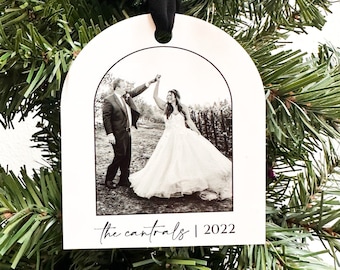 May include: White arched Christmas ornament with a black and white photo of a couple dancing. The ornament has the text "the cantrals | 2022" in a script font and is suspended by a black ribbon.