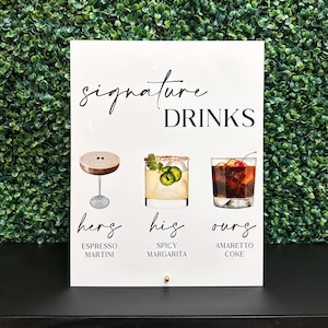 May include: White sign with black text that reads "signature DRINKS".  The sign has three illustrations of cocktails with text below each that reads "hers ESPRESSO MARTINI", "his SPICY MARGARITA", and "ours AMARETTO COKE".