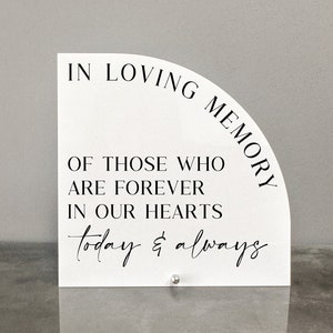May include: White acrylic sign with a half-circle shape. The sign reads "In loving memory of those who are forever in our hearts today & always".
