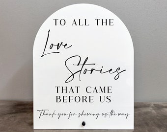 May include: White arch-shaped sign with black text that reads "To all the love stories that came before us. Thank you for showing us the way."