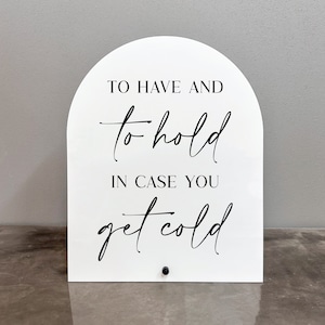 May include: White sign with an arch shape at the top. The sign says "To have and to hold in case you get cold".