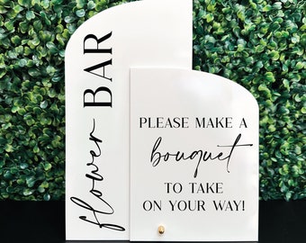 May include: White sign with black text that reads "Flower Bar" and a second white sign with black text that reads "Please make a bouquet to take on your way!"
