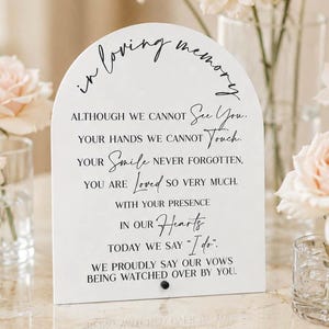 May include: An arched white memorial sign featuring black text that reads: In loving memory, ALTHOUGH WE CANNOT See You. YOUR HANDS WE CANNOT Touch. YOUR Smile NEVER FORGOTTEN. YOU ARE Loved SO VERY MUCH. WITH YOUR PRESENCE IN OUR Hearts TODAY WE SAY "I do". WE PROUDLY SAY OUR VOWS BEING WATCHED OVER BY YOU.