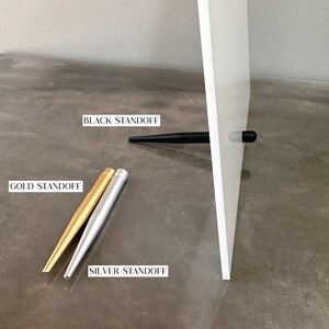 May include: Three standoffs for a picture frame. One is black, one is gold, and one is silver.