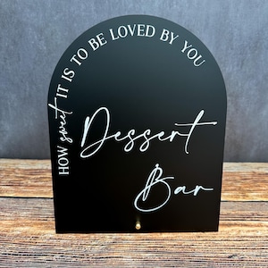 May include: Black arched sign with white text that reads "How sweet it is to be loved by you Dessert Bar".