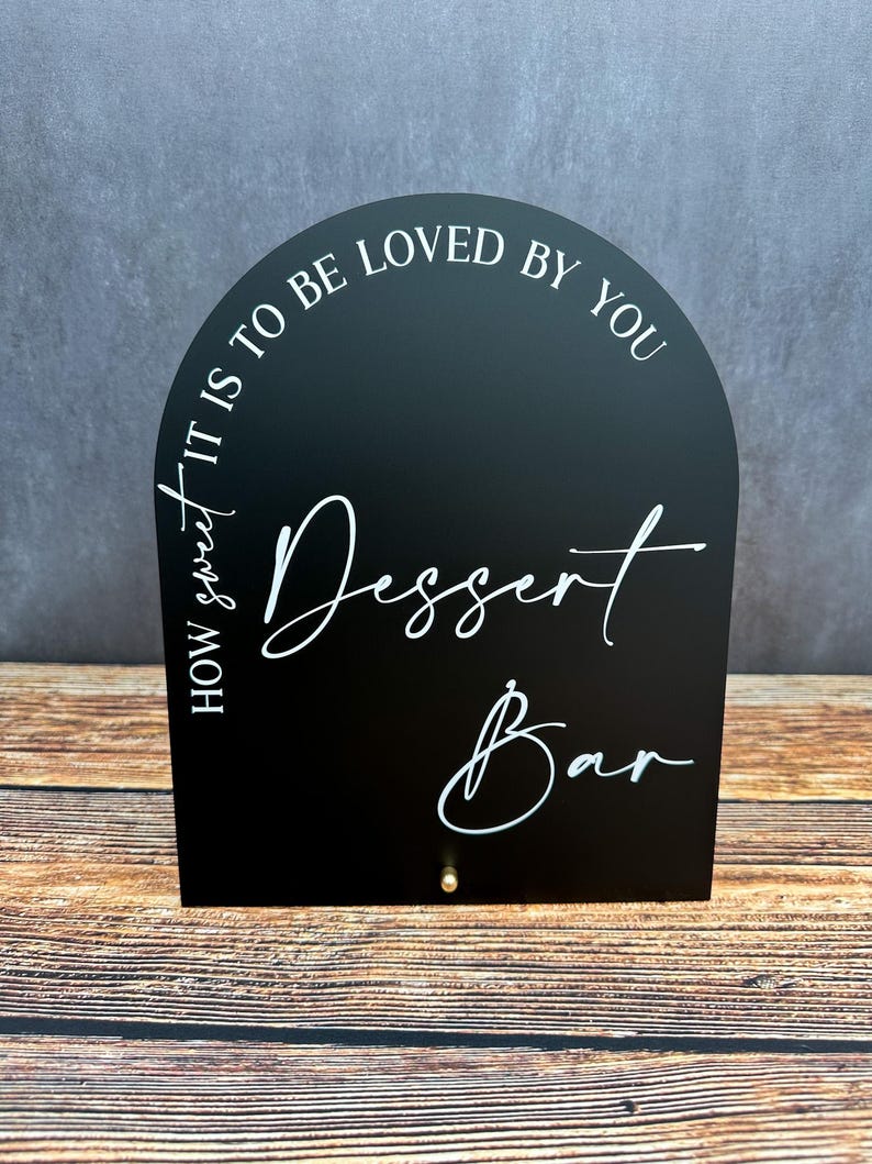 May include: Black arched sign with white text that reads "How sweet it is to be loved by you Dessert Bar".