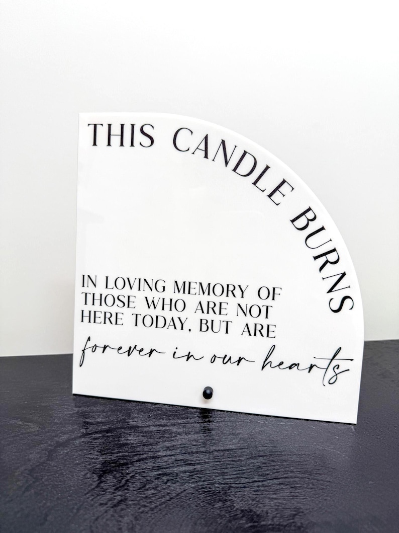 May include: A white, semi-circular memorial plaque with black text that reads "THIS CANDLE BURNS" and "IN LOVING MEMORY OF THOSE WHO ARE NOT HERE TODAY, BUT ARE forever in our hearts." A small black accent is at the bottom.