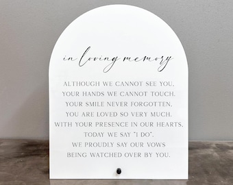 Op de afbeelding: Een wit, boogvormig bord met zwarte tekst die "in loving memory" luidt. De tekst gaat verder met een gedicht over het gedenken van een geliefde tijdens een bruiloft.