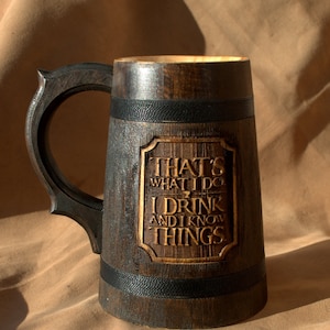 Puede incluir: Una jarra de cerveza de madera marrón oscuro con una banda negra alrededor de la parte superior e inferior. La jarra tiene una inscripción tallada que dice "That's what I do I drink and I know things."