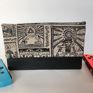 May include: A black Nintendo Switch dock with a fabric cover featuring a black and white illustration of a video game theme. The cover is placed between a blue and a red controller.