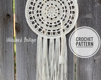 May include: A white crochet dreamcatcher with a circular design and a long fringe. The dreamcatcher is hanging on a wooden fence. The text "CROCHET PATTERN" is visible in a circle on the right side of the image.