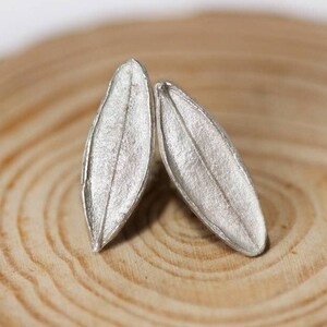 May include: A pair of silver leaf-shaped earrings on a wooden surface.