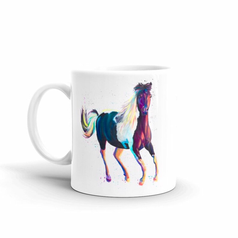 Puede incluir: Taza de cer&aacute;mica blanca con una pintura colorida de un caballo corriendo. El caballo tiene un pelaje blanco y negro con una cabeza y una crin marrones.