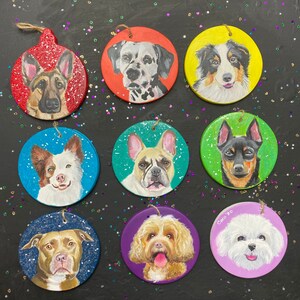 May include: Nine round Christmas ornaments with painted portraits of different dog breeds. The ornaments are painted on a white background with a variety of colors, including red, green, blue, purple, and yellow. The dogs are all smiling and looking at the camera.