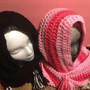 May include: Two crocheted hooded scarves with tassels. One scarf is black and the other is pink and red.