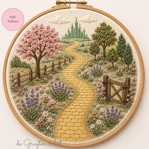 Puede incluir: Arte de paisaje bordado en un aro de madera. La escena representa un camino de ladrillos amarillos que conduce a un castillo verde, con árboles, flores y una valla de madera. El texto "PDF Pattern" está en un círculo rosa.