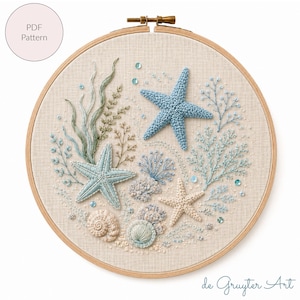 Op de afbeelding: Een ronde houten borduurring met een stoffen paneel met een handgeborduurde maritieme scène. Het ontwerp bevat drie zeesterren in blauw en crème, diverse zeewierplanten in groen en blauw, twee schelpen en kleine blauwe lovertjes.