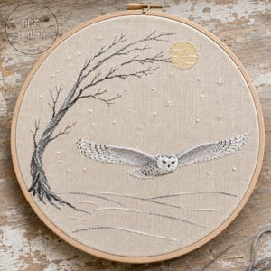 以下が含まれることがあります： 木製の円形刺繍枠に、手刺繍で施された飛行中の白いフクロウ、裸の木、淡い黄色の月、小さな白い星のようなアクセントが描かれたリネン生地。左上にPDF patternというテキストが記載されています。
