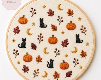 May include: A round wooden embroidery hoop containing a cream-colored fabric with hand-stitched motifs including orange pumpkins, black cats, red and brown autumn leaves, yellow crescent moons, small stars, and brown berry sprigs on stems.