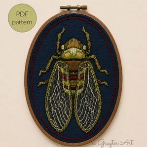 May include: An oval wooden embroidery hoop containing a dark blue fabric with a detailed thread-stitched cicada insect in shades of green, brown, and red. The wings feature intricate white vein patterns. A circular badge reads PDF pattern.