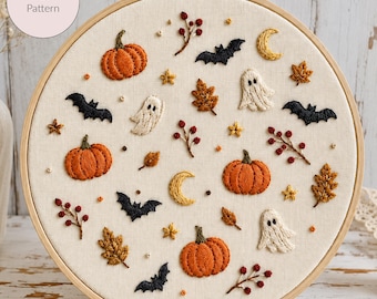May include: An embroidery hoop containing a cream-colored fabric with stitched motifs of orange pumpkins, white ghosts, black bats, yellow crescent moons, brown autumn leaves, and red berry sprigs. A circular label reads PDF Pattern.