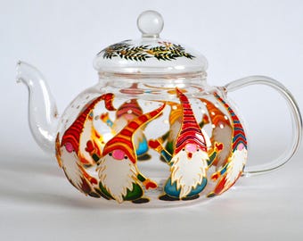 May include: A clear glass teapot featuring a hand-painted design of multiple gnomes with long white beards, pink noses, and colorful pointed hats. The lid is decorated with a green leaf pattern, and the teapot includes a curved handle and spout.
