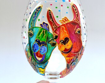 May include: A clear glass wine glass featuring a hand-painted design of two llamas. One llama is colored in vibrant shades of blue and green, while the other is red and orange. The glass is decorated with small, colorful polka dots around the rim.