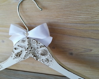 May include: White wooden hanger with a seashell design and a white satin bow. The hanger has the word "unik" written on it.