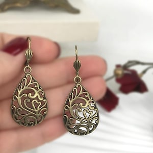 May include: A pair of bronze filigree earrings with a teardrop shape. The earrings have a delicate, intricate design with a floral motif.