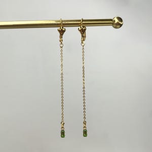 May include: A pair of gold clip-on earrings with a long chain and a small green gemstone at the end of each chain.