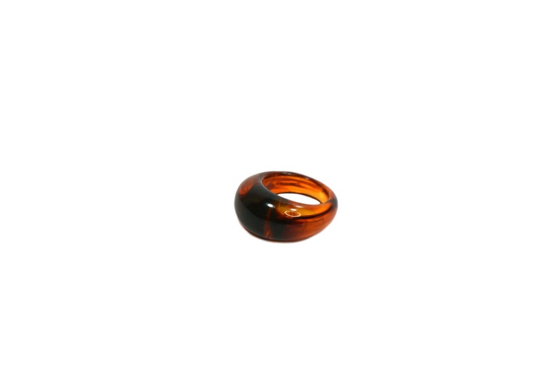 May include: A brown and black resin ring with a rounded, oval shape.