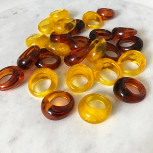 May include: A collection of amber and yellow resin rings. The rings are all different sizes and shapes, and some have a textured finish.