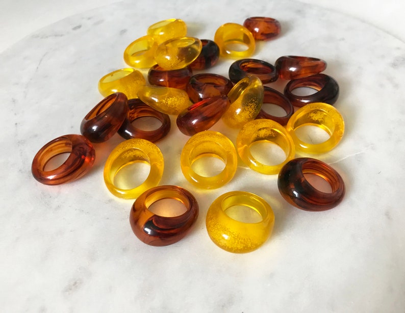 May include: A collection of amber and yellow resin rings. The rings are all different sizes and shapes, and some have a textured finish.