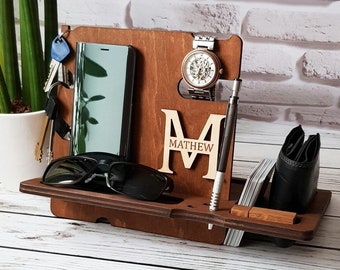 May include: A wooden organizer with a personalized initial "M" and the name "MATTHEW" engraved on it. The organizer has slots for a phone, watch, keys, sunglasses, and a pen.