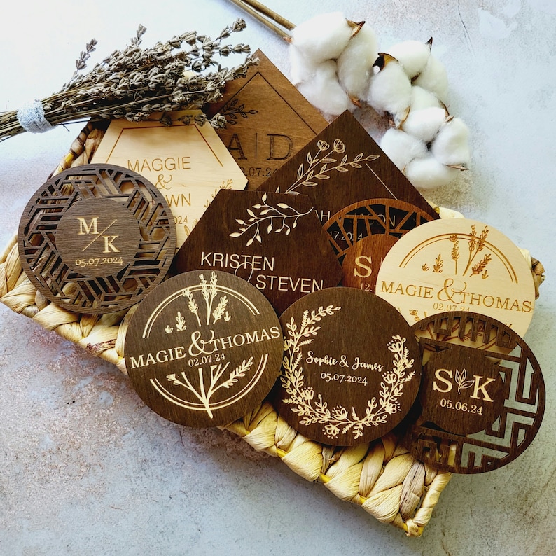 May include: A collection of eight wooden coasters with laser-engraved designs. The coasters feature various floral patterns, initials, and wedding dates. The coasters are arranged in a woven basket.