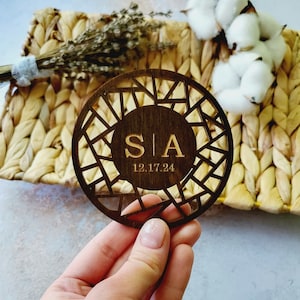 May include: A wooden round coaster with a geometric design and the initials "S|A" and the date "12.17.24" engraved in the center.