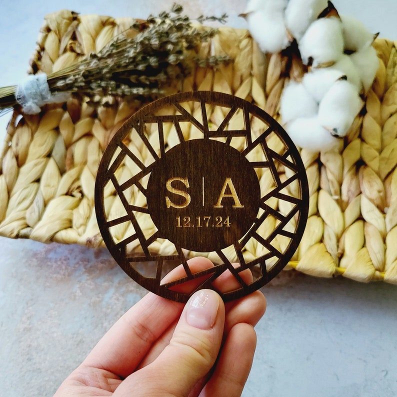 May include: A wooden round coaster with a geometric design and the initials "S|A" and the date "12.17.24" engraved in the center.