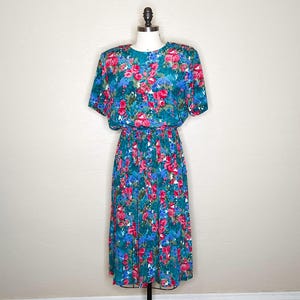 May include: A teal blue midi dress with a floral print featuring pink and blue flowers. The dress has short sleeves and a gathered waist.