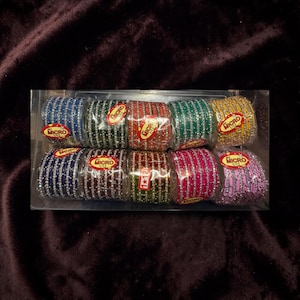 May include: A set of ten stacks of bangles in a clear plastic container. Each stack features a different color including blue, dark green, red, light green, yellow, navy, maroon, olive, pink, and lavender, all accented with silver-toned glitter.