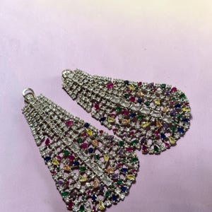 May include: A pair of large, teardrop-shaped statement earrings featuring a silver-toned metal lattice design encrusted with numerous clear, white, and multi-colored gemstones including red, blue, green, and yellow stones in various cuts.