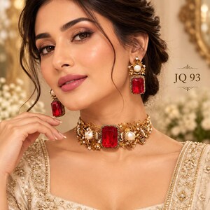 May include: A gold-toned choker necklace and matching drop earrings featuring large rectangular red stones, white pearls, and intricate floral metalwork. The jewelry set is labeled JQ 93 and is worn with a cream-colored garment with gold embroidery.