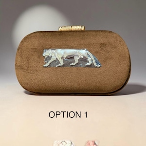 May include: A brown velvet clutch with a silver tiger emblem. The rectangular bag has a gold clasp and the text "OPTION 1" at the bottom. The clutch is a stylish accessory for special occasions.