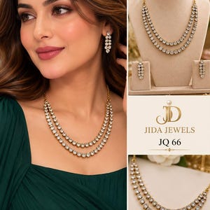 May include: A gold-toned jewelry set featuring a double-strand necklace and matching drop earrings, each adorned with clear round stones. The set is branded JIDA JEWELS JQ 66. The necklace consists of two layered chains with circular stone settings.