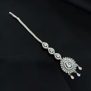 May include: A silver-toned maang tikka headpiece featuring a long chain connected to three oval-shaped links and a large circular pendant. The entire piece is encrusted with clear, sparkling white stones in various cuts, including pear and baguette.