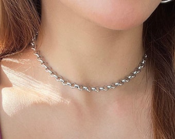 May include: A silver chain choker necklace worn by a person with long brown hair. The necklace is a simple, delicate design.