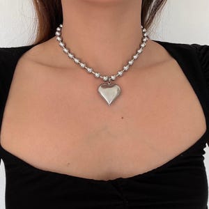 May include: A silver chain necklace with a large heart pendant. The chain is made of small, round beads.