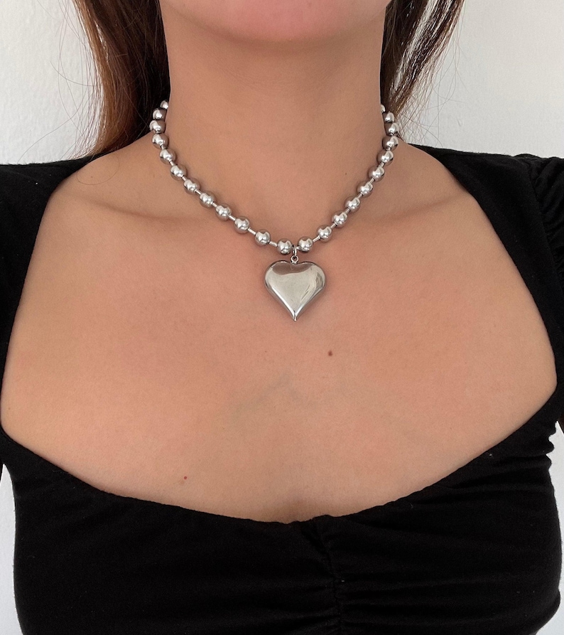May include: A silver chain necklace with a large heart pendant. The chain is made of small, round beads.