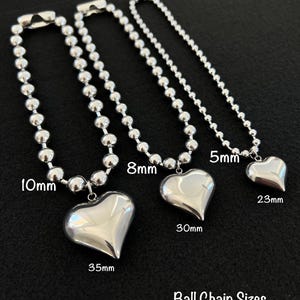 May include: Three silver ball chain necklaces with heart pendants. The chains are 10mm, 8mm, and 5mm in diameter. The heart pendants are 35mm, 30mm, and 23mm in size. Ball Chain Sizes Heart Pendant Sizes