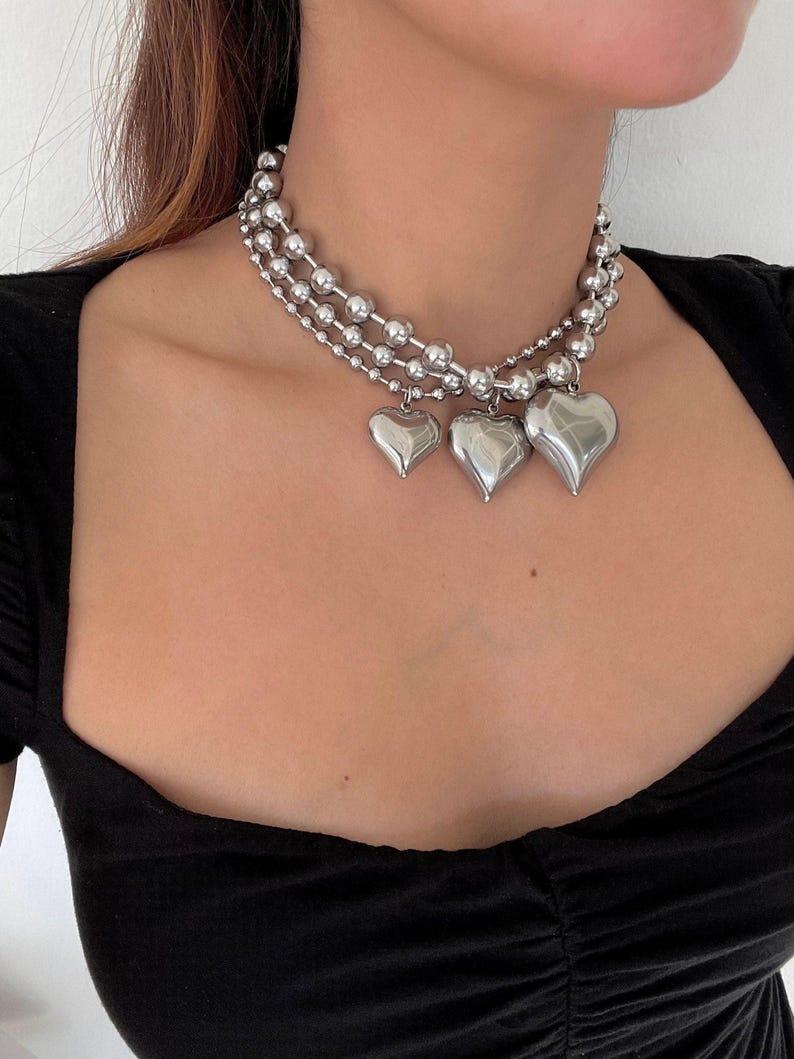 May include: A silver choker necklace with three strands of beads and three heart-shaped charms.